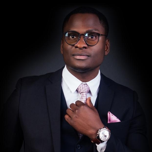 Studio headshot portrait of a man in glasses adjusting his tie