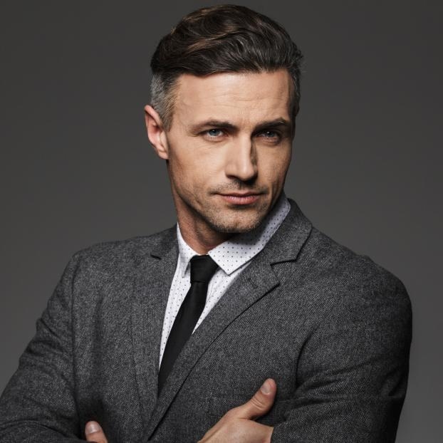 Studio headshot portrait of a man in a gray suit and black tie