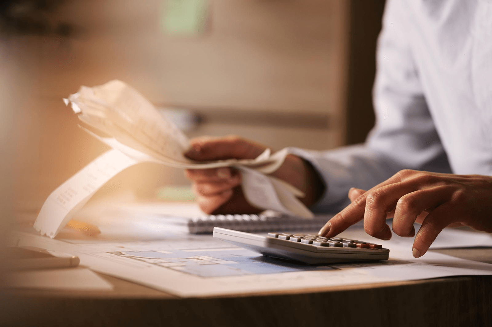 Close-up photo of hands using a calculator with receipts and paperwork on a desk