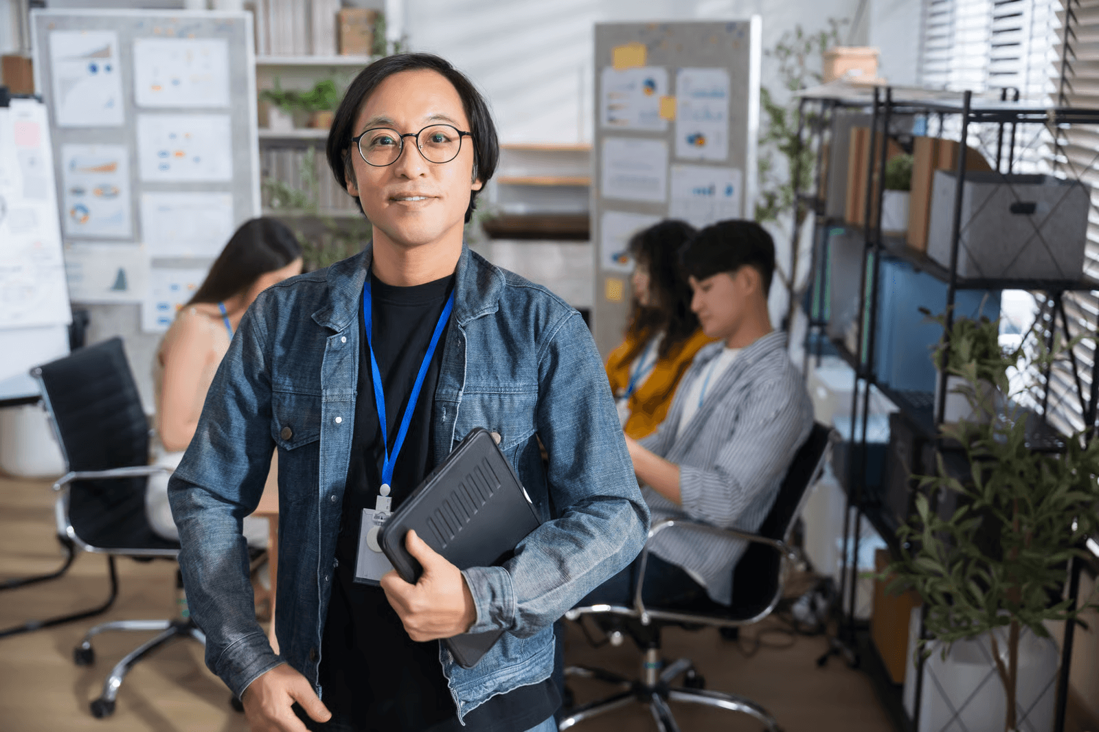 Photo of a man in a denim jacket holding a laptop bag in an office