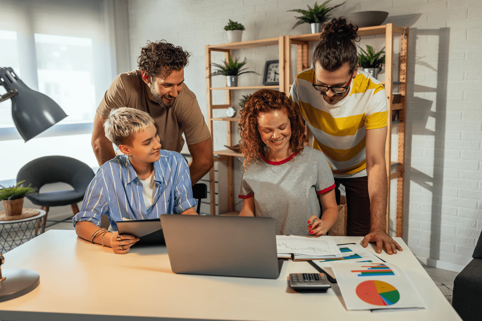Photo of four coworkers smiling around a laptop with charts