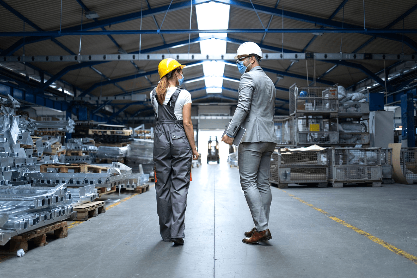 Photo of two people in hard hats and masks walking through a warehouse