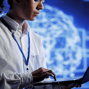Circular photo of a man with a lanyard using a laptop against a glowing globe backdrop