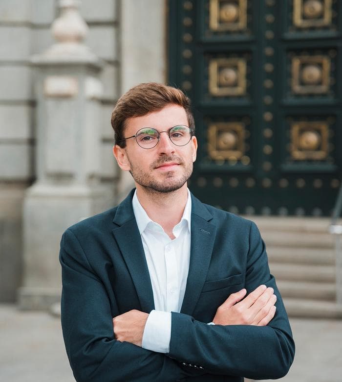 Headshot of a man in glasses standing outside ornate doors