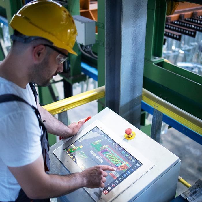 Photo of a factory worker in a yellow hard hat using a touchscreen panel