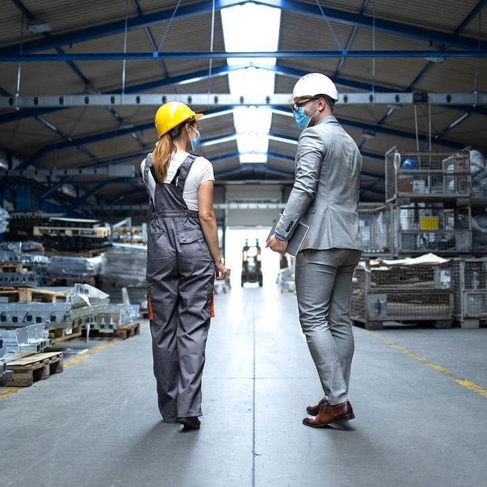 Photo of two people in hard hats and masks walking through a warehouse