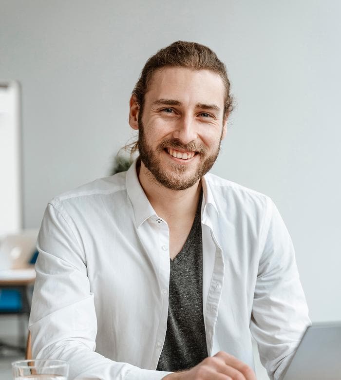 Headshot of a smiling man with a ponytail and beard in a white shirt